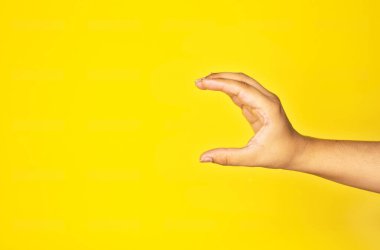 Sağlam sarı bir duvara dayanmış, alıcı bir pozisyonda uzanan eli gösteren keskin bir stüdyo görüntüsü. Bu çok yönlü çerçeve grafik örtüleri, açılır pencere metni veya ürün gösteriminin AR simülasyonları için kullanılabilir.