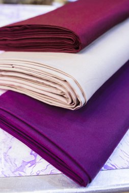 Güzel katlanmış üç kumaş cıvatasının yakın çekim görüntüsü zengin bordo, bej ve koyu mor renkler sergiliyor. Dokular pürüzsüz ve kıvrımlar, maddenin kalitesini vurguluyor..