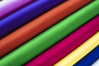 Büyüleyici çapraz düzende sıralanmış renkli kumaş rulolarının yakın görüntüsü, gökkuşağı desenleri ve gölgeler sergiliyor..