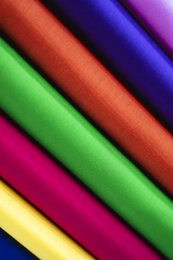 Çapraz katmanlı doymuş kumaşların yakın çekim görüntüsü yoğun bir renk yelpazesi sergiliyor: koyu kırmızı, canlı yeşil, fuşya pembesi, güneş ışığı sarısı ve kraliyet moru. Doku pürüzsüz ve ince bir şekilde yansıtıcı..