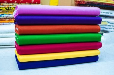 Renkli kumaş rulolarından oluşan düzgünce dizilmiş bir koleksiyon sergileniyor. Ekmekler çeşitli zengin renkleri gösteren gökkuşağı sırasına göre dizilmiştir: mor, mavi, paslı turuncu, yeşil, kırmızı, sarı ve altta koyu mavi.. 