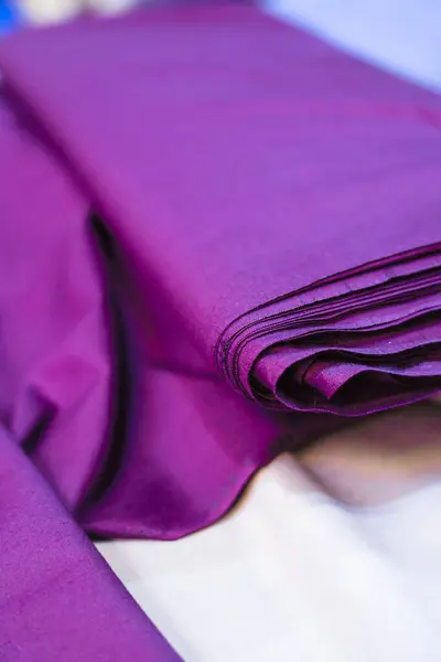 Koyu mor bir kumaş parçasının yakın çekim görüntüsü. Maddenin dokusu pürüzsüz ve rengi de yoğun. Altında bir parça beyaz kumaş görünüyor..