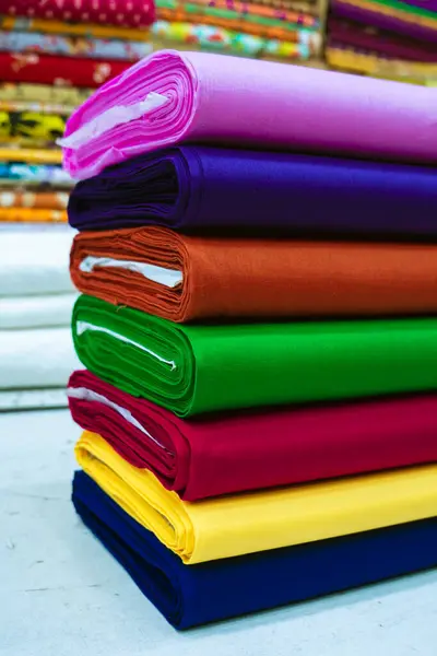 Çeşitli tonlarda renkli kumaş yığını, çeşitli doku ve renkler sergiliyor. Ekmekler düzgünce düzenlenmiş, tekstilin zengin renklerini vurguluyor..