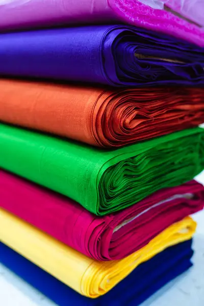 Mor, mavi, turuncu, yeşil, pembe, sarı ve mavi gibi çeşitli zengin renkleri içeren sarılmış kumaş yığınının yakın çekim görüntüsü. Ruh hali, basit ve parlak bir arkaplan üzerine kurulmuş canlı ve dokudur..