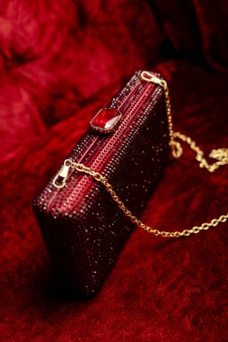 Lüks bir kırmızı kristal el çantası zarif bir şekilde kırmızı kadife bir fonda sergileniyor. Çanta parlak kırmızı kristallerle süslenmiş, titizlikle yüzeyi boyunca dizilmiş, göz kamaştırıcı bir etki yaratıyor.. 