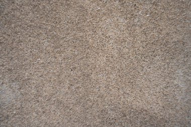 Bej çakıl taşı çizgi duvar dokusunun yakın görüntüsü. Yüzey açık kahverengi bir çimento tabanına gömülü küçük çakıl taşlarından oluşur ve hafif kaba ve granüler bir görünüm oluşturur. Görüntü boyunca renk tutarlı.