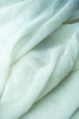 Soluk, soluk beyaz bir kumaşın, ince tırtıklı bir dokusu var. Kumaş yumuşak bir şekilde örtülmüş, zarif kıvrımlar ve kıvrımlar oluşturuyor. Işık yüzeyden nazikçe yansıyarak kumaşın hassas parıltısını ve dokusunu vurgular. Desenleme için ideal