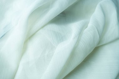 Soluk renkli, yumuşak kıvrımlı ve kıvrımlı kumaşın yakın çekim görüntüsü. Malzeme hafif ve muhtemelen saf görünüyor.