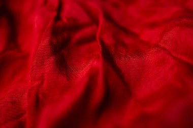 Büyüleyici bir yakın çekim. Lüks kırmızı bir kumaşın karmaşık dokusunu ve koyu kırmızı rengini ortaya çıkarıyor. Yumuşak kıvrımlar ve gölgeler dramatik ve zarif bir görüntü yaratır.