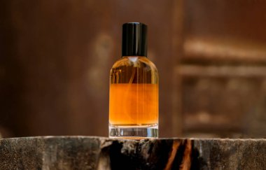 Siyah şapkalı cam parfüm şişesinin yakın plan görüntüsü. Şişe kehribar renkli bir sıvıyla dolu, bu da zengin ve muhtemelen sıcak bir koku olduğunu gösteriyor. Yıpranmış, koyu kahverengi bir tahta parçasına dayanıyor, muhtemelen bir ağaç kütüğü ya da kütüğün bir kısmına.,