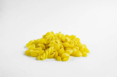 Beyaz arka planda pişmemiş küçük bir koni makarnasının yakın çekim görüntüsü. Makarna parlak sarı ve kabuk şeklinde. Makarnaya odaklanmış, yüzeysel bir alan derinliği arkaplanı hafifçe bulanıklaştırıyor. Çakmak.