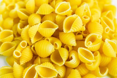 Pişmemiş bir koni makarnasının detaylı, yüksek çözünürlüklü yakın çekim fotoğrafı. Makarna parlak sarı ve her bir parça açıkça görülebilir. Kabuk şeklini ve dokusunu sergiliyor.