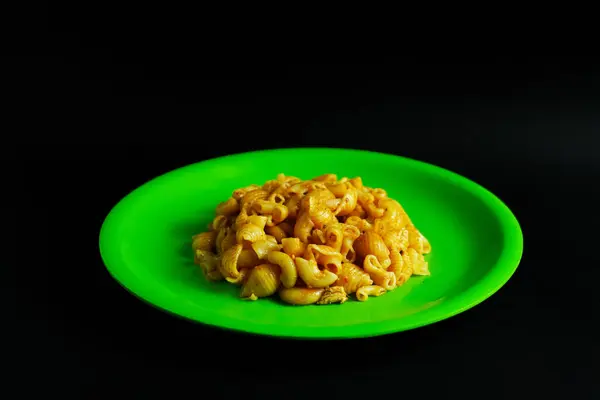 Işıl ışıl yeşil bir tabakta servis edilen pişmiş makarnanın titiz bir yakın plan çekimi. Resim, yiyeceklerle ilgili çeşitli bağlamlarda kullanıma uygun basit ama görsel olarak çekici bir besin sunumu sunmaktadır.