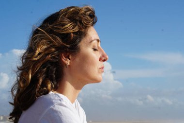 Kumsaldaki esmer kadın, bulutlu mavi gökyüzüne karşı yaz gününün tadını çıkarıyor. 
