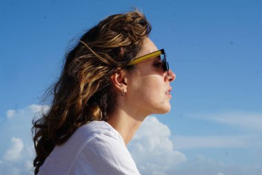 Kumsaldaki esmer kadın, bulutlu mavi gökyüzüne karşı yaz gününün tadını çıkarıyor. 