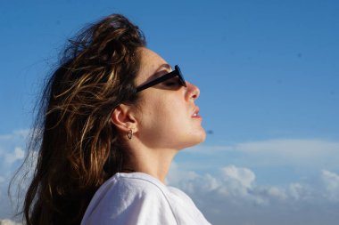 Kumsaldaki esmer kadın, bulutlu mavi gökyüzüne karşı yaz gününün tadını çıkarıyor. 