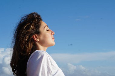 Kumsaldaki esmer kadın, bulutlu mavi gökyüzüne karşı yaz gününün tadını çıkarıyor. 