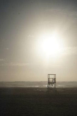 Kumlu sahilde ahşap cankurtaran kulesi, okyanusun üstünde günbatımı gökyüzü. 