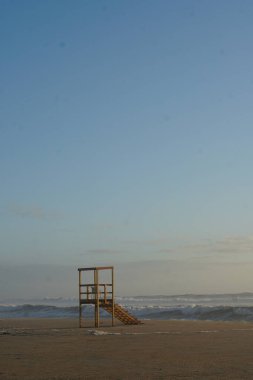 Kumlu sahilde ahşap cankurtaran kulesi, okyanusun üstünde günbatımı gökyüzü. 