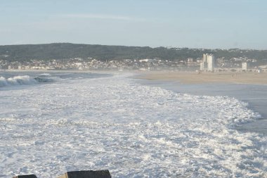 Okyanus dalgaları ve arka planda şehir. Portekiz, Figueira da Foz