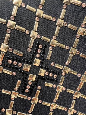 Siyah taban renginde bir kumaşa takılmış altın boncukların dikey fotoğrafı. Daha lüks ve zarif görünüyor.