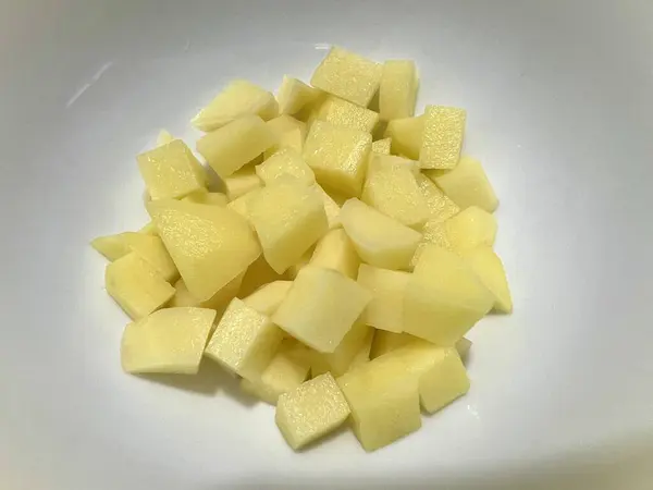 Küçük parçalara ayrılmış taze soyulmuş patatesler, beyaz arka planda izole edilmiş.