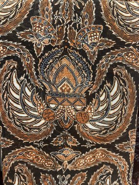 Geleneksel Endonezya batik kumaşının dikey fotoğrafı, bir tacı andıran soyut bir motifle. Siyah, kahverengi ve beyaz renklerin birleşimiyle.