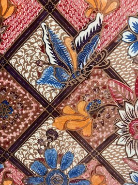 Geleneksel Endonezya batik kumaşının dikey fotoğrafı, etrafındaki yapraklar ve çiçekler üzerinde uçan ve tüneyen güzel kelebeklerin motifi..