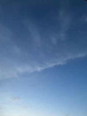 Mavi gökyüzünün iki parçaya bölünmüş gibi görünen güzelliğinin dikey fotoğrafı. Yumuşak beyaz bulutların dalgaları onu kaplamaya başlıyor..