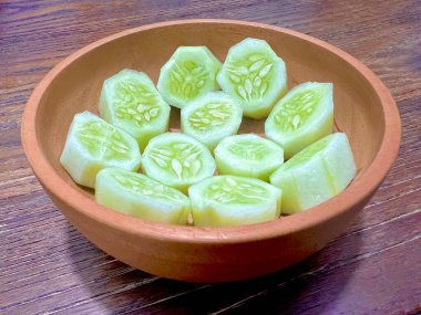 Tahta bir kasede dilimlenmiş salatalıklar hazır, yakın plan çekilmiş, ahşap bir masada.