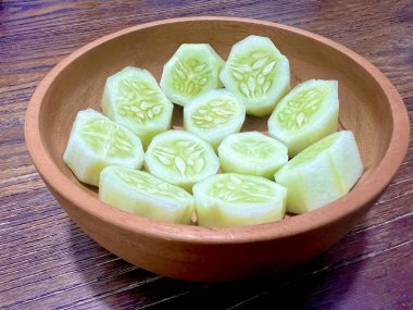 Tahta bir kasede dilimlenmiş salatalıklar hazır, yakın plan çekilmiş, ahşap bir masada.