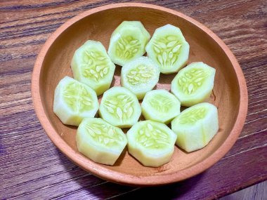 Tahta bir kasede dilimlenmiş salatalıklar hazır, yakın plan çekilmiş, ahşap bir masada.