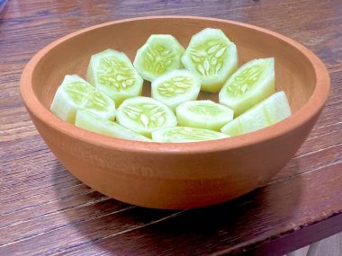 Tahta bir kasede dilimlenmiş salatalıklar hazır, yakın plan çekilmiş, ahşap bir masada.