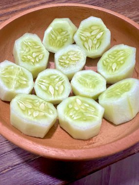 Tahta bir kasede dilimlenmiş salatalıklar hazır, yakın plan çekilmiş, ahşap bir masada.