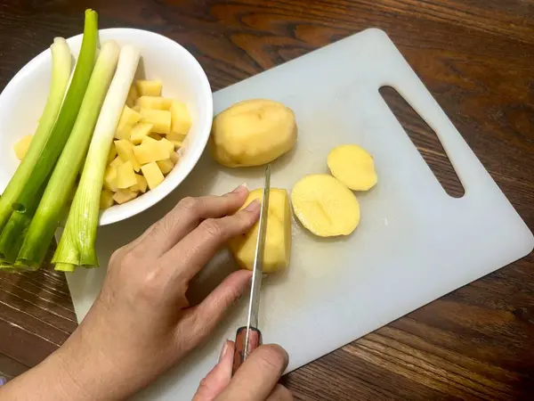 Yemek pişirme hobisi olan kadın mutfak tahtasına sebze, patates ve pırasa kesiyor.