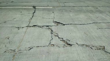 Ağır çatlamış beton yol yüzeyinde gözle görülür çatlaklar ve bozulma izleri var. Hasar, stres, yük veya kötü malzeme kalitesi nedeniyle düzensiz bir yapısal bozulma şekli oluşturuyor..