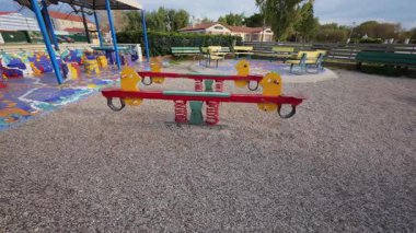 Yalnız bir tahterevalli, boş bir oyun parkında, sıralar ve çakıllarla çevrili duruyor. Çocukların yokluğu, izolasyon ve nostaljiyi ima ederken geçmiş oyun zamanlarını hatırlatıyor..