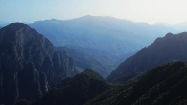 Hava aracı görüntüleri iki yüksek tepe arasında yükselen bir dağ silsilesini yakalıyor..
