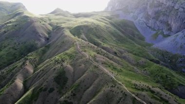 Uçsuz bucaksız tepeler, devasa bir dağ ve gün batımının aydınlattığı bir patika..