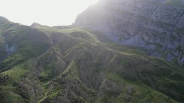 Gün batımında devasa bir dağın altındaki yeşil ovalar ve tepelerin hava görüntüleri..