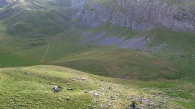 Güneşli bir ovada yürüyüş yolu her iki tarafında tepeler ve gölgeler bırakan büyük bir dağ..
