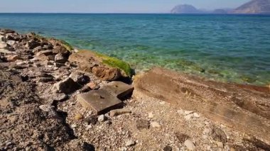 Temiz suları olan manzaralı bir sahil moloz ve taşlarla kaplıdır. Doğal güzelliği geri getirmek için acil temizlik gerekli..