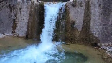 Geleneksel taş duvar barajı, şelale ve yapay gölet içeren kırsal bir nehir manzarası..