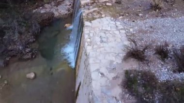 Doğal bir gölet, taştan bir duvarın üzerinden taştan bir nehre dökülen, bir vadideki kayalar ve yemyeşil sularla çevrili bir su gibi oluşur..