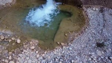 Taştan bir baraj, barışçıl bir gölet ve çevresindeki bitki örtüsünden oluşan bir şelaleyi gösteren kayalık bir nehrin insansız hava aracı görüntüleri..