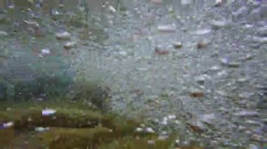 Su altı görüntülerinde temiz su ile kayalık bir nehir yatağı görülüyor. Kabarcıklar ve yüzey sıçramaları görünüyor..