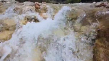 Sualtı perspektifi, kayaların arasından akan suyun yavaş çekimde küçük bir şelaleye düştüğünü gösteriyor..