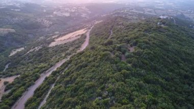 Yunanistan 'da çekilen bu hava görüntülerinde yeşil Akdeniz ormanları ve bir dağ yamacındaki tarım arazileri boyunca uzanan toprak yollar görülüyor.