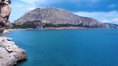 Yunanistan 'da Akdeniz suyu ve kayalık dağlar tarafından bir deniz kenarı oteli görülebilir. Kumsal ve dağınık ağaçlar doğal bir kıyı şeridi oluşturur..