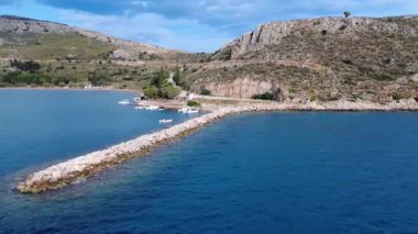 Yunanistan 'dan gelen bu kıyı sahnesi taştan bir dalgakıranla korunan kayalık bir koy gösteriyor. Sakin turkuaz su sığınakları engebeli denizden gelen küçük balıkçı tekneleri.